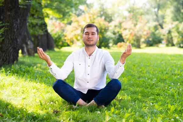 若い男は緑の芝生の上で蓮のポーズで瞑想します 閉じた目でヨガの練習をカジュアルな服装でハンサムな男 夏の日にトレーニングと瞑想の屋外 健康的なライフスタイルとリラクゼーション — ストック写真