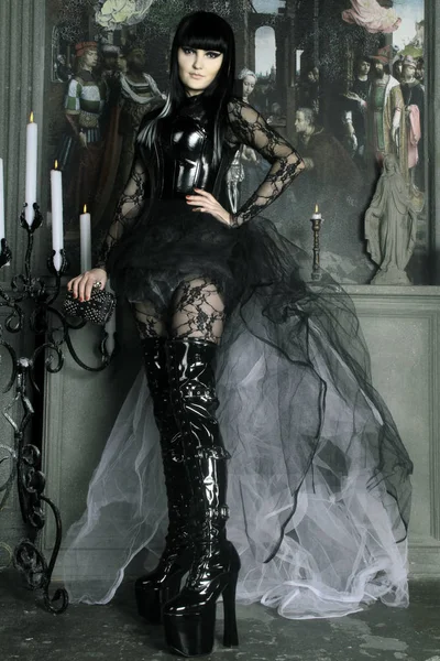 Mooie jonge gotische meisje dragen zwarte pvc en lace kleding poseren met kaarsen in het oude kasteel — Stockfoto