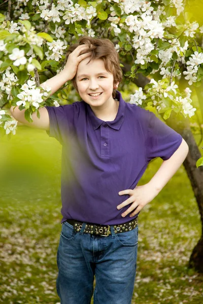 Αρκετά ευγενική παιδί αγόρι στέκεται και χαμογελαστός στον κήπο λουλούδια δέντρο μήλο — Φωτογραφία Αρχείου