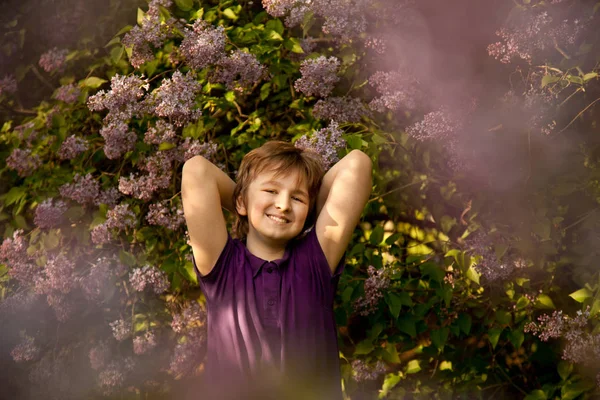 Joli garçon gentil souriant dans les lilas dans le jardin d'été — Photo