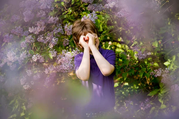 Joli garçon gentil souriant dans les arbres lilas et montrant coeur d'amour symbole par ses paumes dans le jardin d'été — Photo