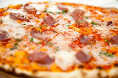 Beyaz ahşap masa üzerinde peynir ve sığır sosis ile lezzetli sıcak pizza
