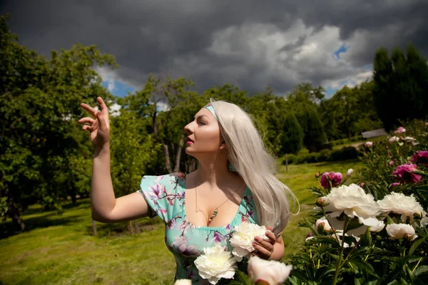 Bella capelli lunghi donna bionda nel parco dei fiori estivi cinque minuti per la pioggia — Foto Stock