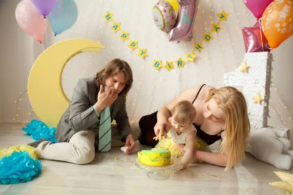 little baby birthday one year girl crushing her yellow cake wth mother and father