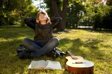 teen boy outdoors with a guitar, a book and an apple on sunset in the park having fun clipart