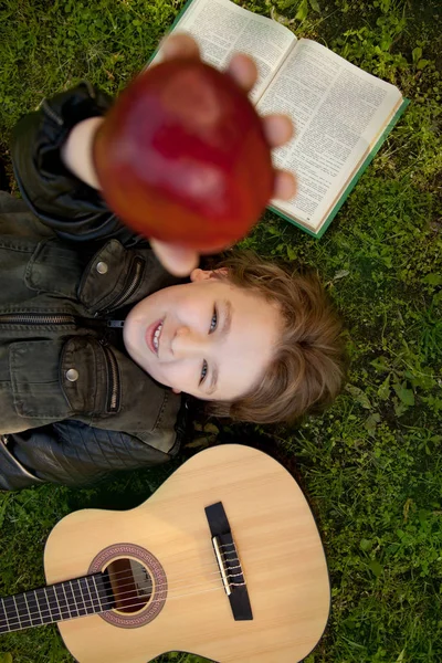 Adolescente ao ar livre com uma guitarra, um livro e uma maçã no pôr do sol no parque se divertindo — Fotografia de Stock