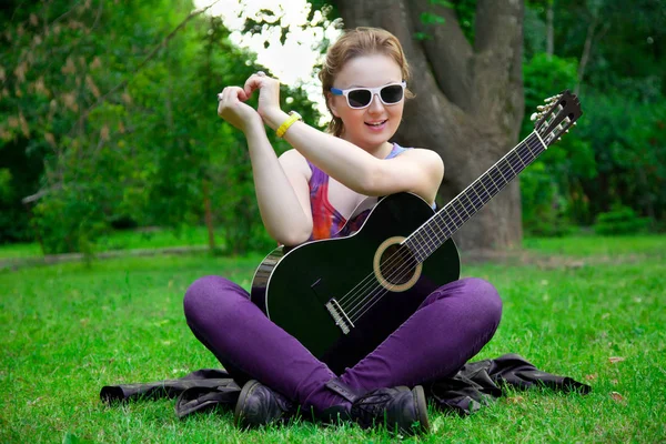 Ładna kobieta z czarny gitara w parku — Zdjęcie stockowe