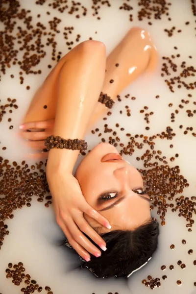 Belle femme dans le bain de lait avec des grains de café — Photo
