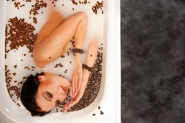 Vacker kvinna i mjölk badet med kaffebönor — Stockfoto