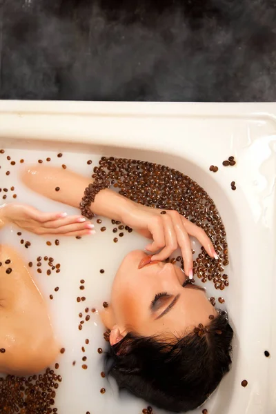 Красивая женщина в молочной ванне с кофейными зёрнами — стоковое фото