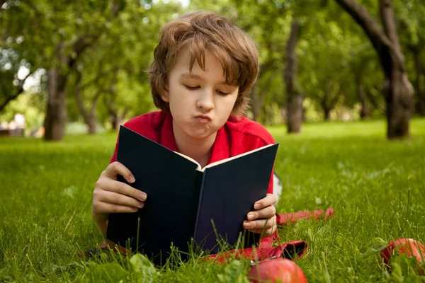 Triste aburrido sorprendido adolescente chico leyendo un libro en el verde verano manzanos parque — Foto de Stock