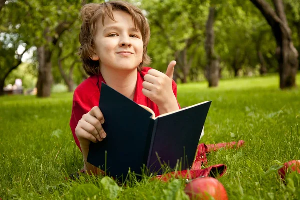 Adolescente chico leyendo un libro en el verde verano manzanos parque — Foto de Stock