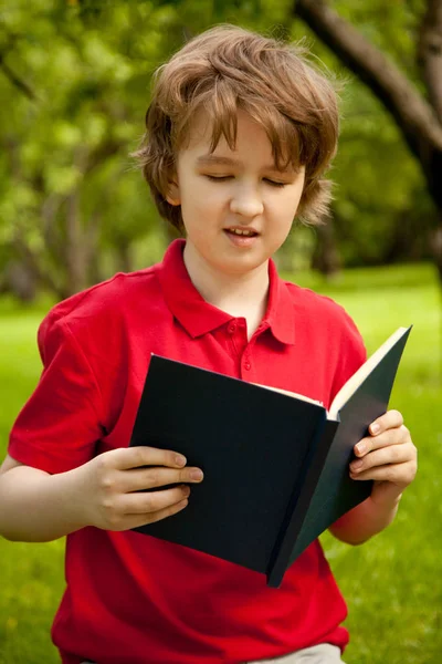 Adolescente chico leyendo un libro en el verde verano manzanos parque — Foto de Stock