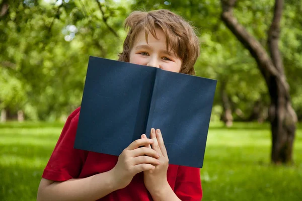 Tiener jongen lezen van een boek in het groene zomer apple bomen park — Stockfoto