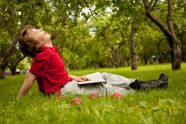 Adolescente chico leyendo un libro en el verde verano manzanos parque — Foto de Stock