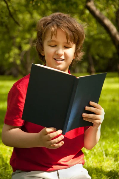 Adolescente chico leyendo un libro en el verde verano manzanos parque — Foto de Stock