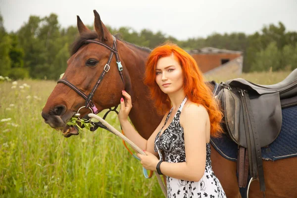 Orange hair woman and her brown horse in the field just relaxing in summer day — стоковое фото