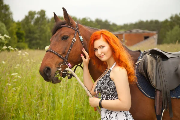 Orange hair woman and her brown horse in the field just relaxing in summer day — стоковое фото