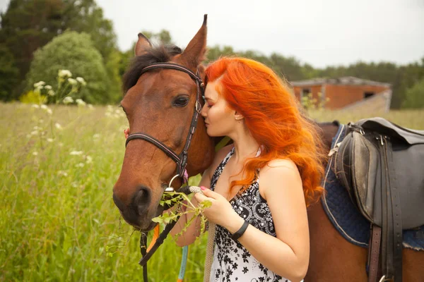 Oranžové vlasy žena a její hnědé koně v poli relaxování v letním dni — Stock fotografie