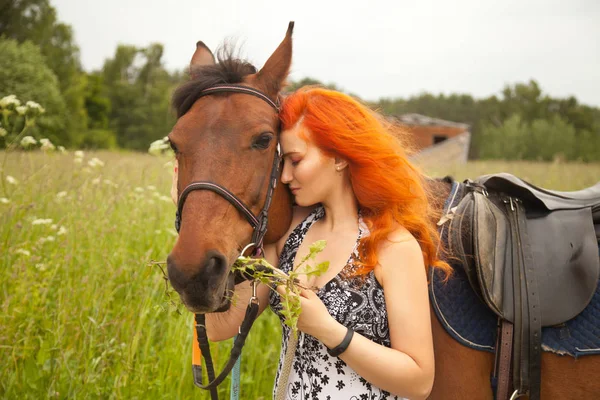 Oranžové vlasy žena a její hnědé koně v poli relaxování v letním dni — Stock fotografie