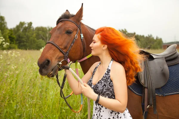 Помаранчева жінка волосся і її коричневий кінь в полі просто розслабляється в літній день — стокове фото