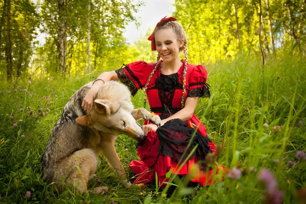 Hübsches Mädchen in rotem Kleid sitzt mit dem Hund Wolf auf dem Gras im Wald — Stockfoto