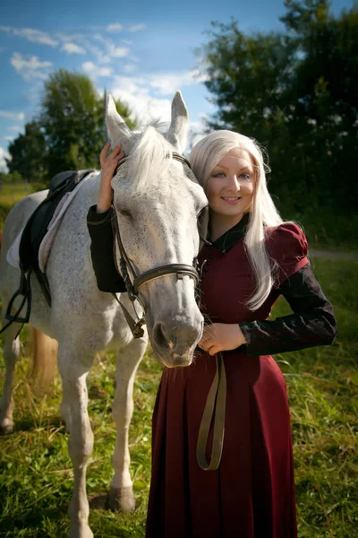 Ziemlich schöne Frau mit langen blonden Haaren und ihrem Freund Pferd im Freien im Sommerdorf — Stockfoto