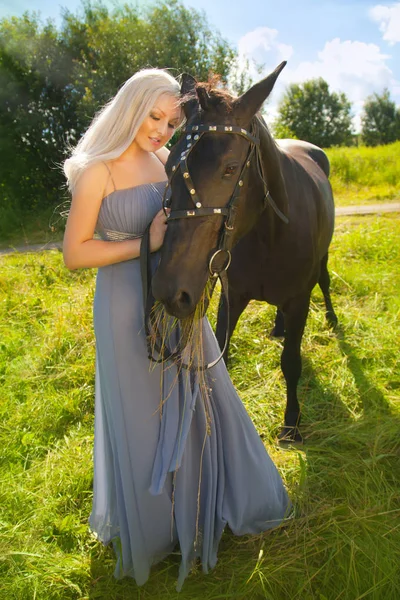 Ziemlich schöne Frau mit langen blonden Haaren und ihrem Freund Pferd im Freien im Sommerdorf — Stockfoto