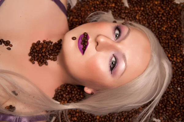 Beautiful blonde woman lying with coffee beans top view — Stock Photo, Image