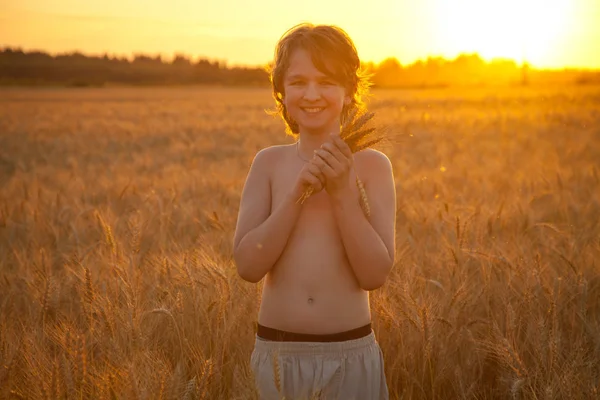 Menino feliz muito sorridente no campo de trigo por do sol com buquê — Fotografia de Stock