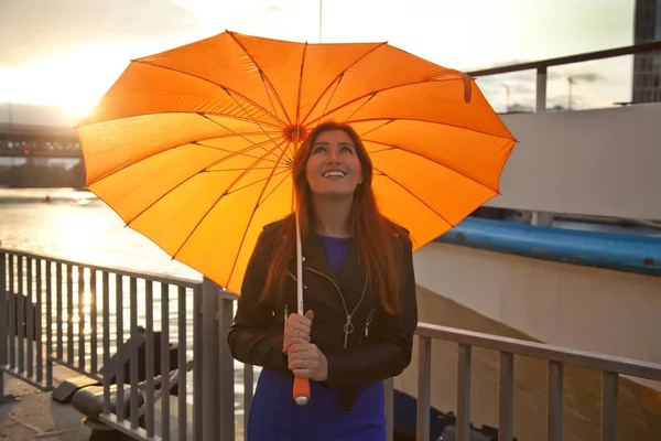 Красивая молодая рыжая женщина с оранжевым большим зонтиком на городской улице — стоковое фото