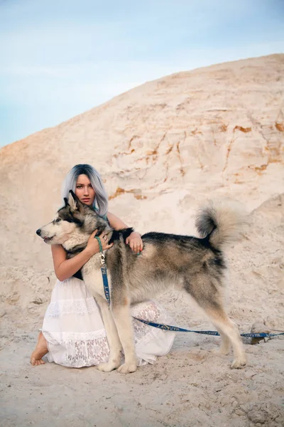 Bela jovem dona e sua linda feliz malamute cão na pedreira deserto areia branca — Fotografia de Stock