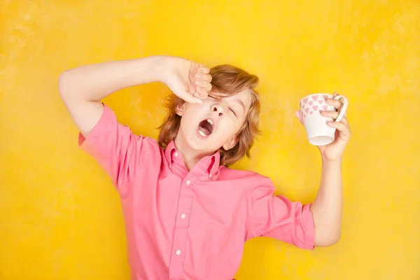 Έφηβο φοράει ροζ πουκάμισο στέκεται πάνω σε κίτρινο φόντο στο στούντιο και χασμουρητό με πρωινό καφέ — Φωτογραφία Αρχείου