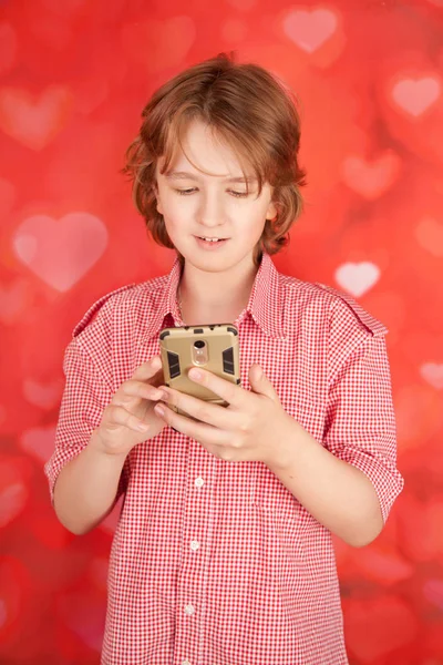 Красивый симпатичный молодой мальчик с мобильным смартфоном на фоне красных сердец только в студии — стоковое фото