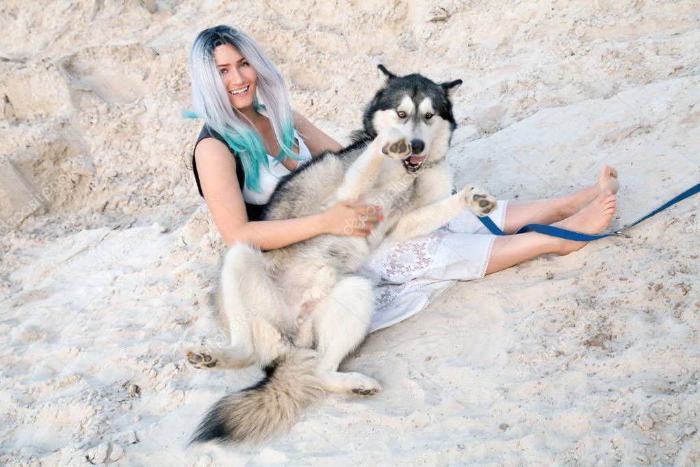 beautiful young woman owner and her lovely happy dog malamute in the desert quarry white sand
