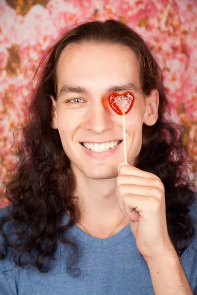 Przystojny romantyczny młody człowiek z czerwonym sercem candy osamotniony w studio z różowym tle — Zdjęcie stockowe