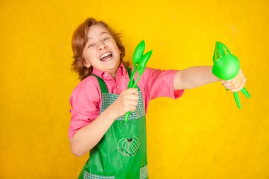 komik genç çocuk çocuk sarı arka plan üzerinde pembe gömlek ve yeşil önlük giyiyor. mutfak mücadele.