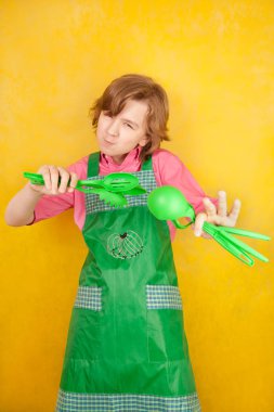 komik genç çocuk çocuk sarı arka plan üzerinde pembe gömlek ve yeşil önlük giyiyor. mutfak mücadele.