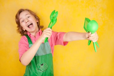 komik genç çocuk çocuk sarı arka plan üzerinde pembe gömlek ve yeşil önlük giyiyor. mutfak mücadele.