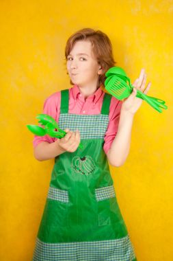 komik genç çocuk çocuk sarı arka plan üzerinde pembe gömlek ve yeşil önlük giyiyor. mutfak mücadele.