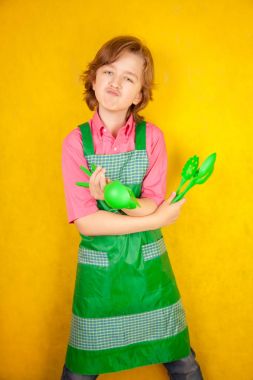 komik genç çocuk çocuk sarı arka plan üzerinde pembe gömlek ve yeşil önlük giyiyor. mutfak mücadele.