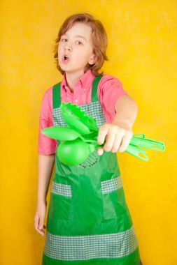 komik genç çocuk çocuk sarı arka plan üzerinde pembe gömlek ve yeşil önlük giyiyor. mutfak mücadele.