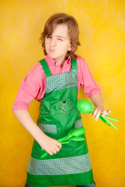 komik genç çocuk çocuk sarı arka plan üzerinde pembe gömlek ve yeşil önlük giyiyor. mutfak mücadele.