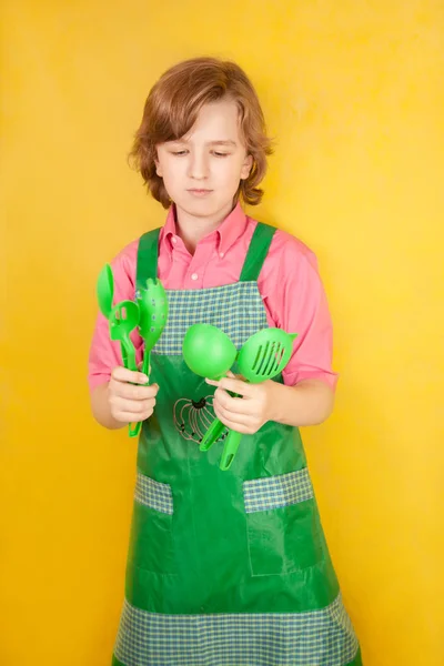 Αστείος αγόρι παιδί φοράει ροζ πουκάμισο και πράσινη ποδιά στο κίτρινο φόντο. κουζίνα αγώνα. — Φωτογραφία Αρχείου