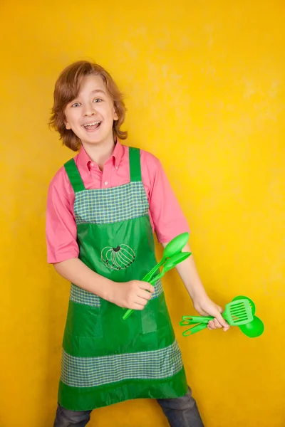 Смішний молодий хлопчик у рожевій сорочці та зеленому фартуху на жовтому тлі. кухонний бій . — стокове фото