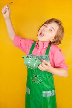 çorba tabağı ve bir kaşık ile yeşil mutfak önlük ayakta giyen güzel çocuk