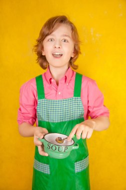çorba tabağı ve bir kaşık ile yeşil mutfak önlük ayakta giyen güzel çocuk