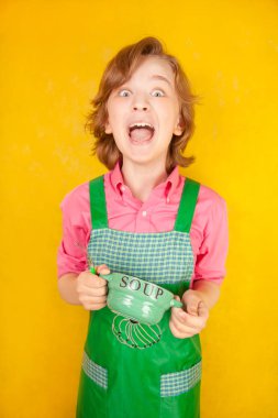 çorba tabağı ve bir kaşık ile yeşil mutfak önlük ayakta giyen güzel çocuk