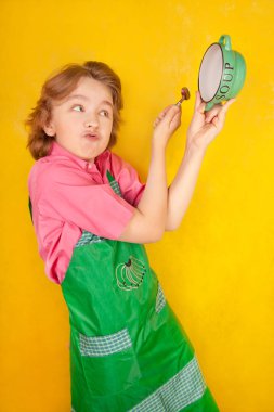 çorba tabağı ve bir kaşık ile yeşil mutfak önlük ayakta giyen güzel çocuk