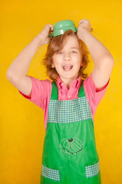 nice child wearing green kitchen apron standing with soup plate and a spoon